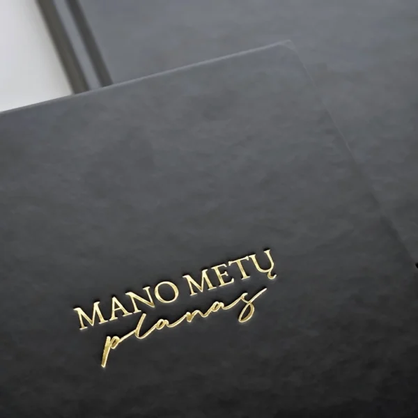 juodas-asmeninio-augimo-planuoklis-auksinis-uzrasas Juodas asmeninio augimo planuoklis „Mano metų planas“ su blizgančiu auksiniu užrašu iš arti.